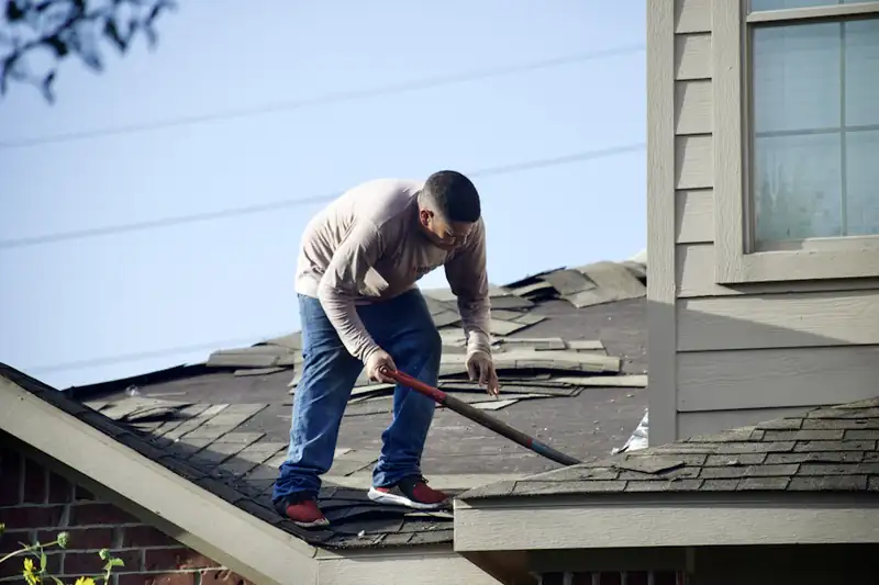 Roofer tearing off old shingles on a residential roof